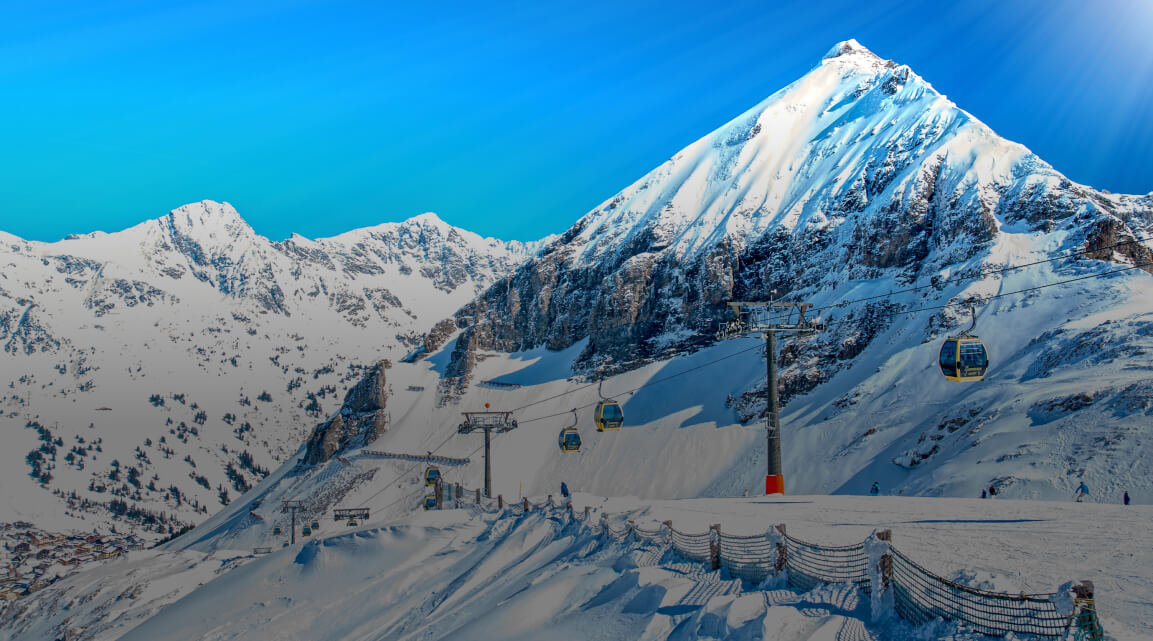 Skilift an einem pittoresken schneebedeckten Berg, dessen Gipfel steil vor einem strahlend blauen Himmel aufragt