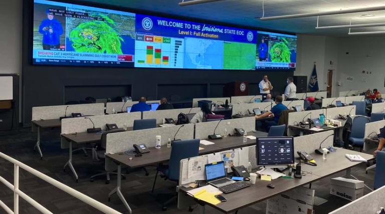 The Louisiana State Emergency Operations Center, with a news feed and GIS dashboards on large screens and analysts working at computers