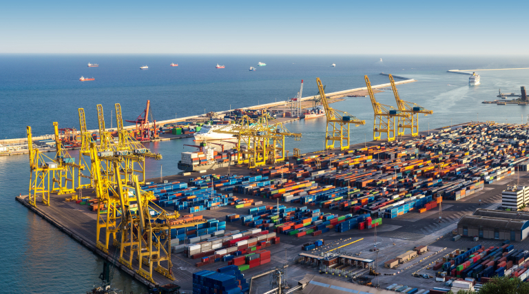 A container port with large stacks of shipping containers, yellow cranes, and cargo ships