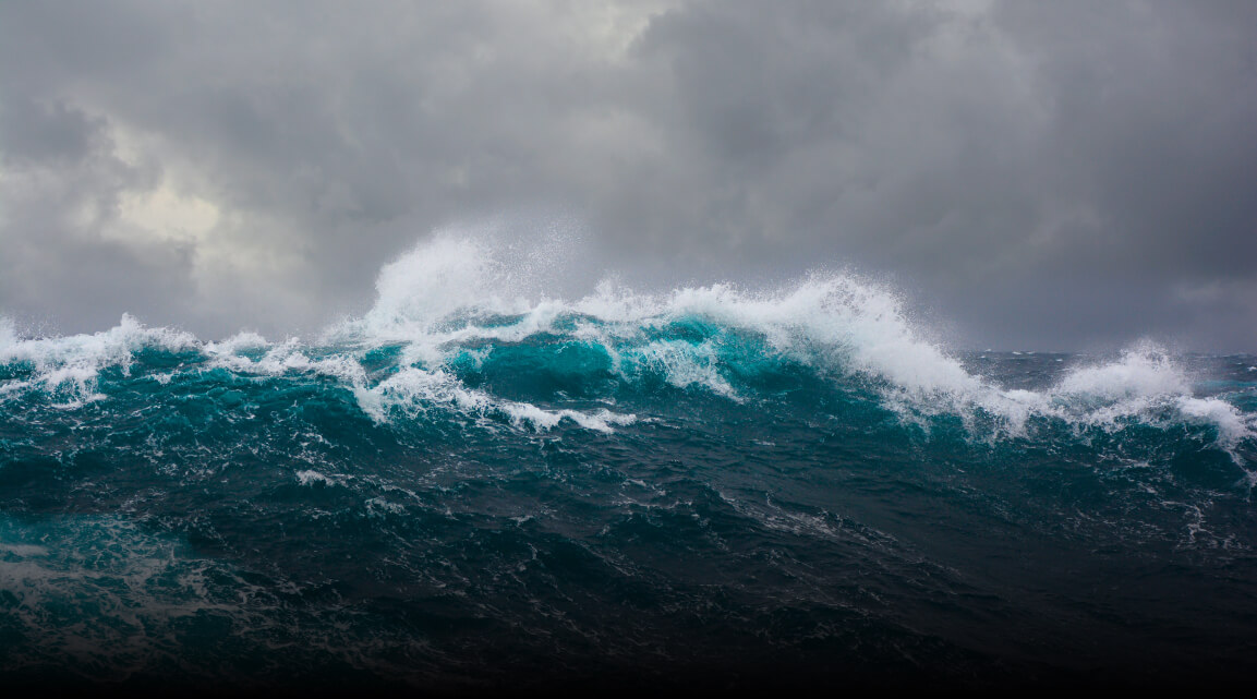 An ocean wave breaking against a dark stormy sky