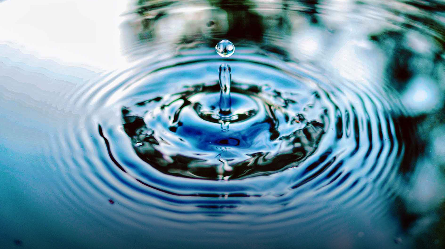 Um close-up de uma gota de água enviando ondulações na superfície de um lago