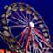 A brightly lit Ferris wheel beside a yellow and red hot dog stand under a dark blue twilight sky