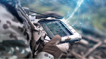 A neck-down view of a uniformed soldier holding a tablet with gloved hands as glowing lines emerge from the screen