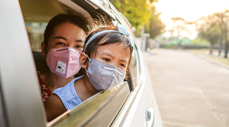 woman holding a child in a car and both are wearing masks