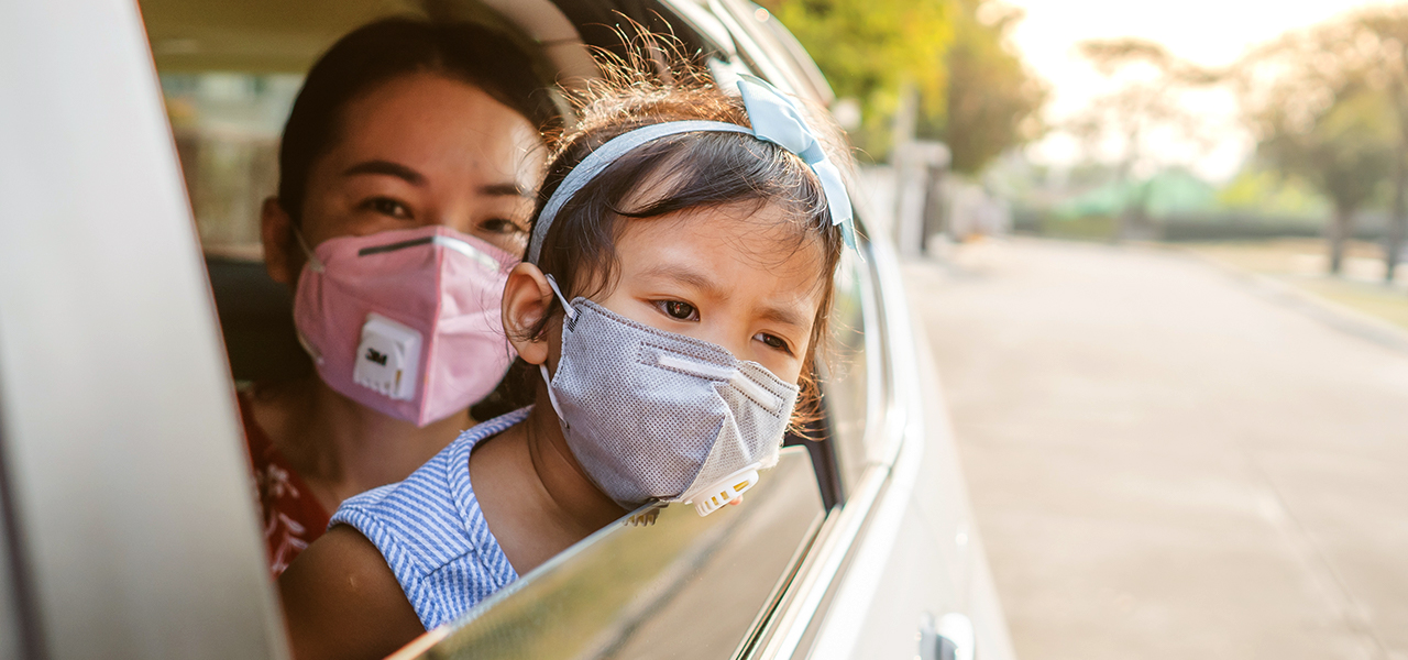 Une femme dans une voiture portant un masque et tenant un jeune enfant portant également un masque