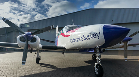 An Ordnance Survey airplane on the ground by a hangar