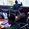 An operations center room with a group of uniformed responders sitting at computer stations with monitors displaying map dashboards and incident data