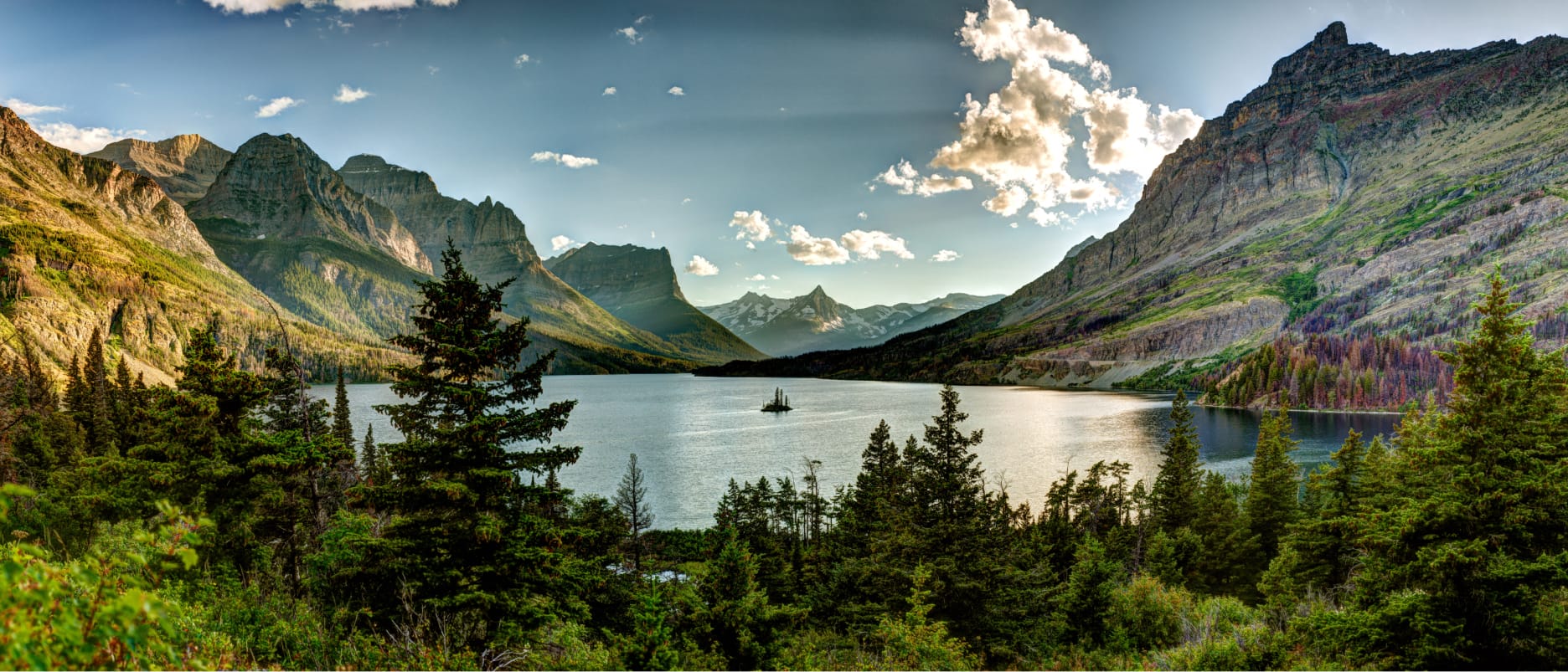 A serene lake surrounded by towering mountains and pine trees under a clear blue sky