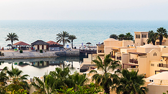 A cluster of Mediterranean-style buildings surrounded by palm trees near the ocean 
