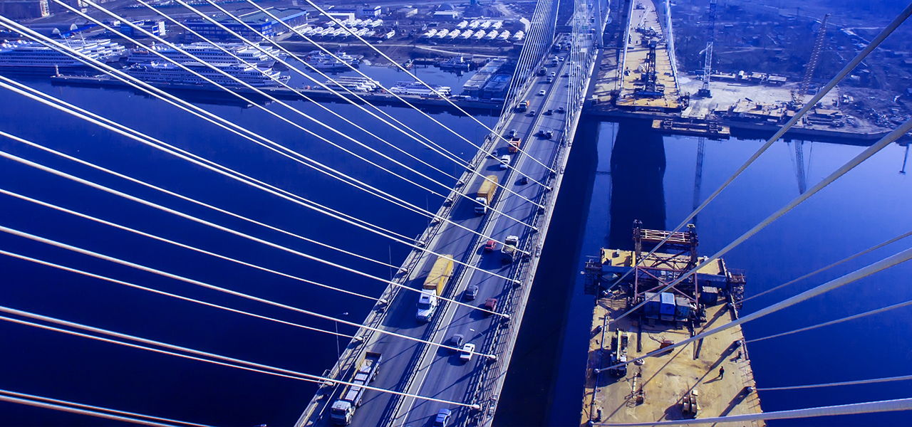 A suspension bridge that spans a body of water with vehicle traffic next to a suspension bridge that is under construction