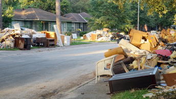 A tree-lined suburban neighborhood with heaps of debris piled up along the curbs in front of each house
