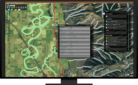 A monitor displaying an application interface that shows an aerial map of fields and mountains