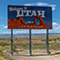 A stretch of interstate highway through wide scrub-covered desert with a large colorful billboard stating “Welcome to Utah” under a bright blue sky