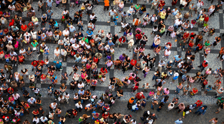 An aerial photo of a colorful crowd of people scattered around a paved public square