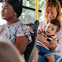 A parent with a child in their lap riding a bus surrounded by other passengers