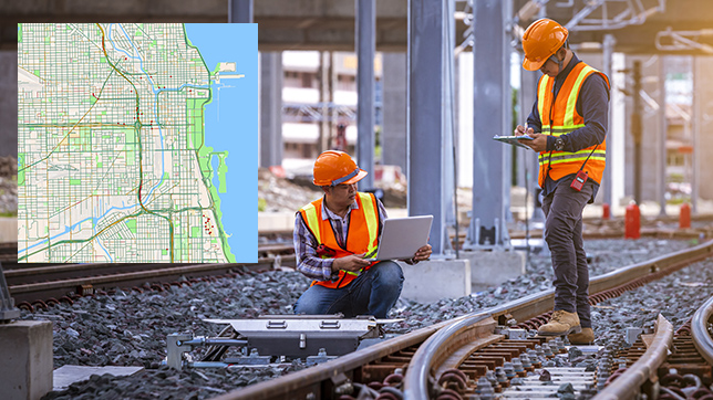 Two workers hold laptops while they look at a rail switch mechanism; a map of a city with rail lines inset to the left