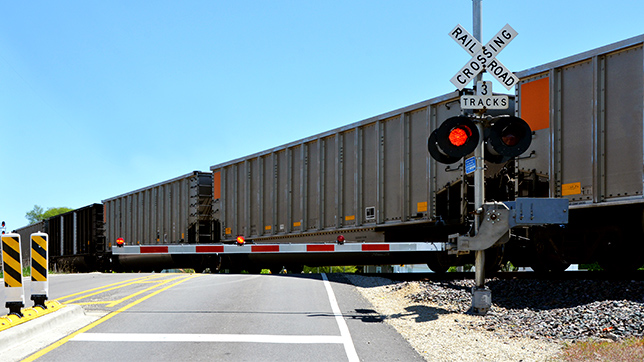 Freight cars crossing a road at a rail crossing with the bars down and the red signal lit
