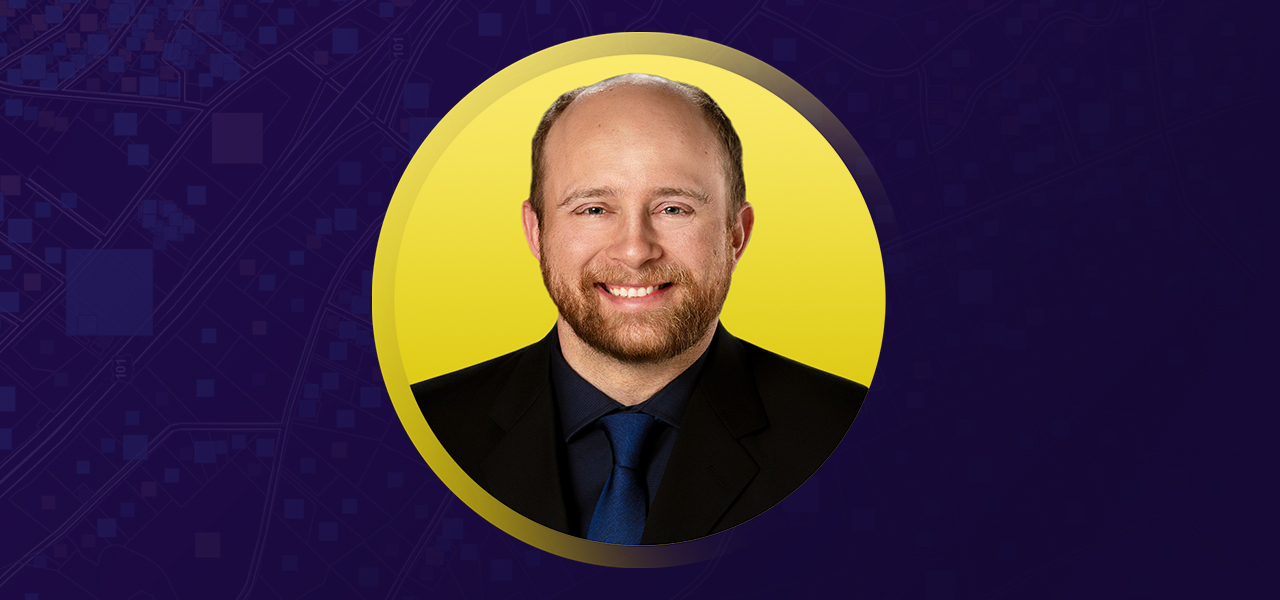Brandon smiling in a suit and tie overlaid on a yellow and purple background