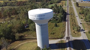 A water tower with trees and a two-lane road in the background