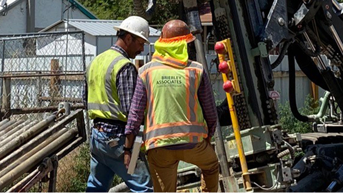 Two people wearing hard hats and yellow safety vests standing outside discussing mining equipment