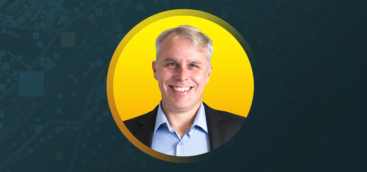 Portrait of Daniel Johns smiling in a dark suit in a sunlit lobby