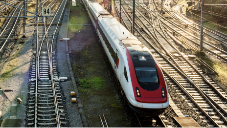 A white and red commuter train moving through a railroad switch area with many tracks in a row