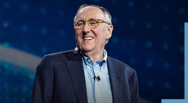 A photo of Jack Dangermond wearing a headset and smiling onstage at a conference