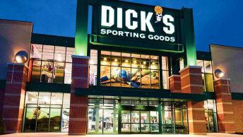 A brightly lit two-story DICK’S Sporting Goods storefront with a deep blue evening sky in the background