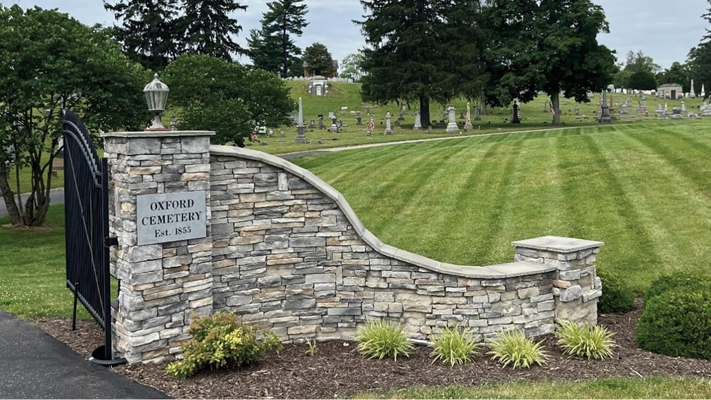 A modern stone-brick entry to the Oxford Cemetery, with rolling green grave-studded hills visible beyond