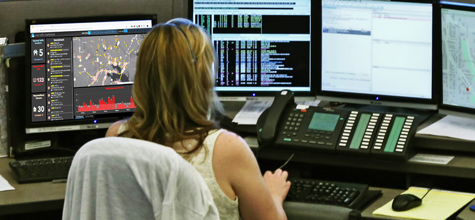 A person sitting in a cubicle working with mapping and data software on multiple monitors