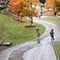 A rainy view of a walkway with people walking through, surrounded by grass, trees, and elevation Repeat Standard Item 1 fields for additional items.