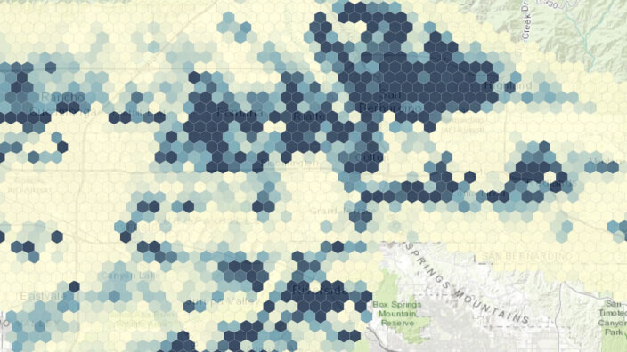 Um mapa verde claro e cinza de uma área montanhosa sobreposto com uma grade opaca amarela e azul de formas hexagonais