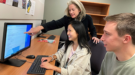 An instructor guiding two students through a GIS course on a desktop computer