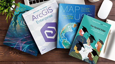 Four Esri Press books scattered on a wooden tabletop