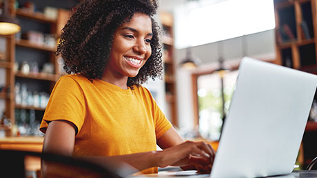 Uma foto de um estudante adolescente sorridente em uma camisa amarela trabalhando em um laptop em um ambiente de biblioteca