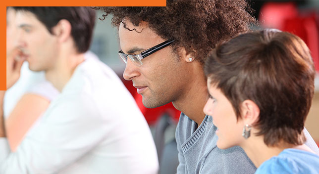 Photo of three casually dressed attendees in a group seminar setting gazing to the left at an unseen speaker or screen