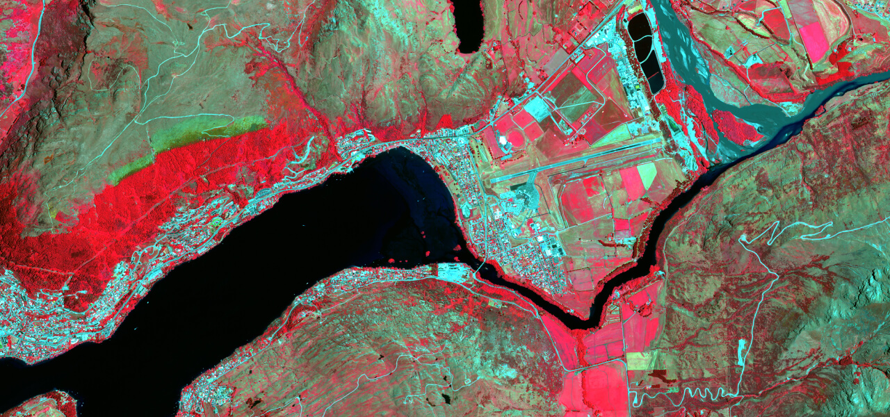 Satellite imagery of a body of water leading into a narrow river surrounded by land highlighted in reds, blues, and greens