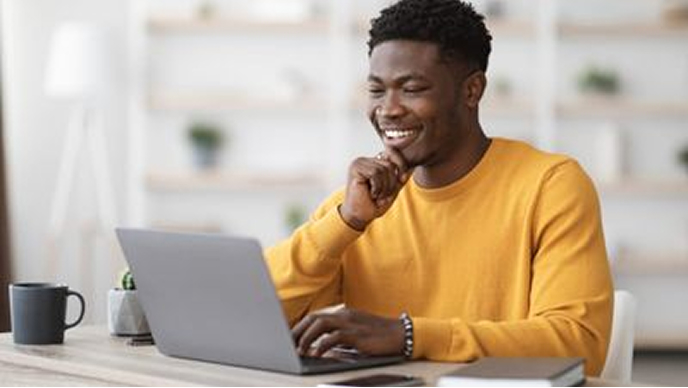 Smiling person in a yellow pullover working on a laptop in an office setting