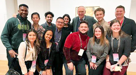 A crowd of student assistants wearing conference lanyards smiling as they pose for a group photo with Jack Dangermond in the middle