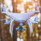 A closeup photo of a large white drone in mid-flight with a thick stand of trees in the unfocused background