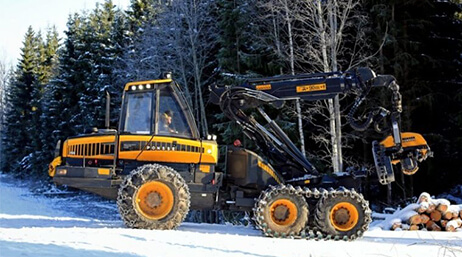 A photo of a piece of yellow and black heavy machinery on a snow-covered road in a winter forest beside a stack of logs