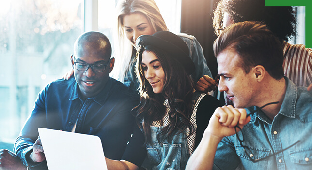 A photo of five casually dressed people grouped around a laptop monitor in a brightly lit room