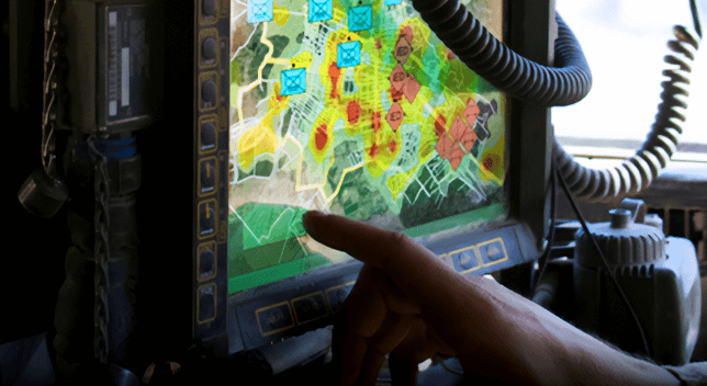 A closeup photo of a human hand with the index finger tapping a wall-mounted screen displaying a colorful map