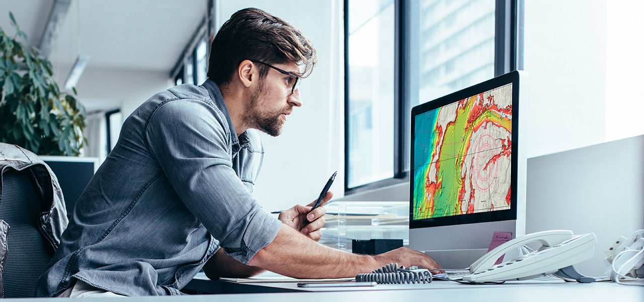 Uma pessoa sentada em uma mesa em um escritório, trabalhando em um computador que exibe um mapa topográfico vibrante