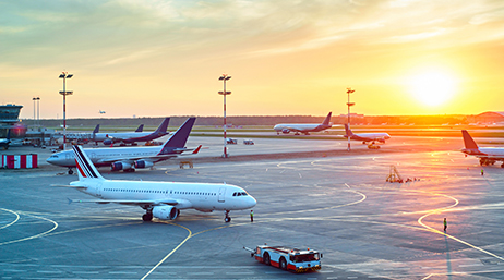 An airfield with scattered airplanes parked on it with a golden sunset in the background