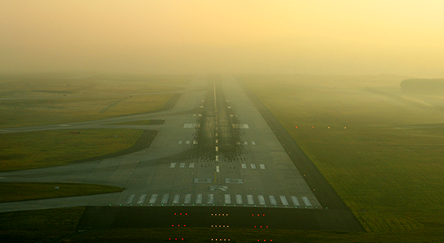 A photo of an airport runway dimly lit beneath a heavily hazy yellow sky