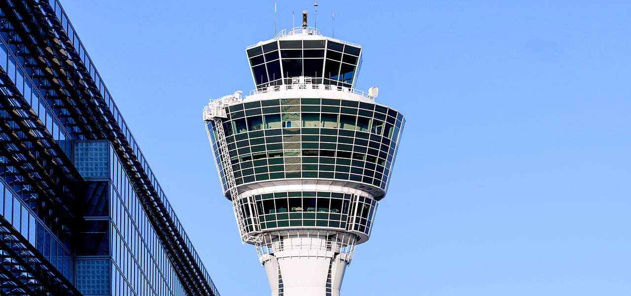 A photo of a white air traffic control tower against a clear blue sky