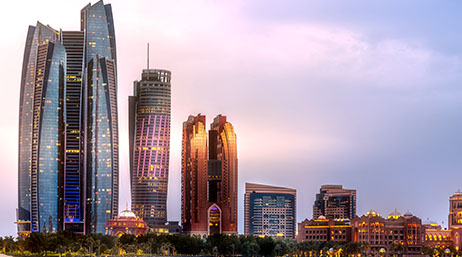 A photo of a row of modern skyscrapers softly lit by a sunrise against a pale blue and pink sky