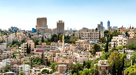 A photo of a city with buildings in white and beige in a tree-filled landscape beneath a clear blue sky