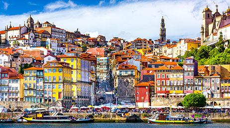 A vibrant coastal city with yellow, red, and white buildings under a partly cloudy sky